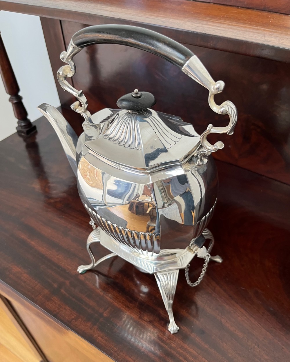 A silver-plated spirit kettle with a fluted lower body, dark wooden handle, gooseneck spout, and matching stand containing an alcohol burner below. View X