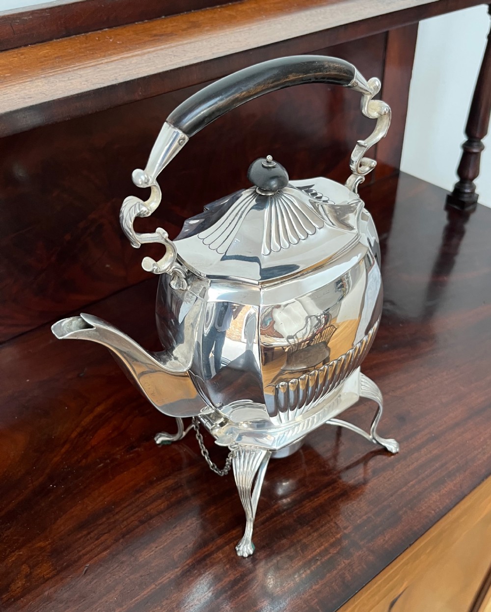 A silver-plated spirit kettle with a fluted lower body, dark wooden handle, gooseneck spout, and matching stand containing an alcohol burner below. View XI