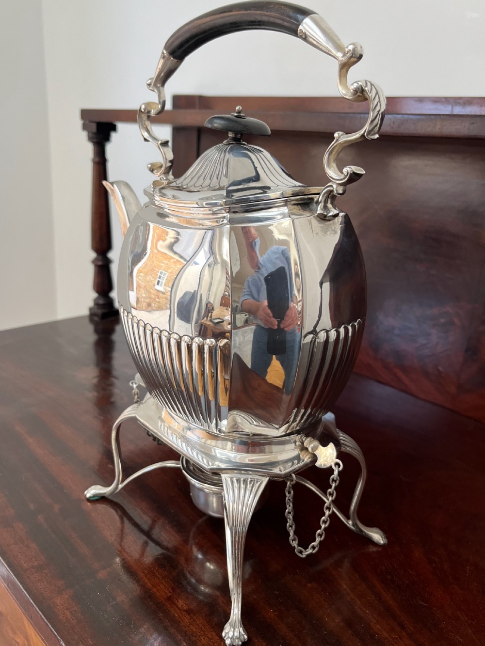 A silver-plated spirit kettle with a fluted lower body, dark wooden handle, gooseneck spout, and matching stand containing an alcohol burner below. View XII