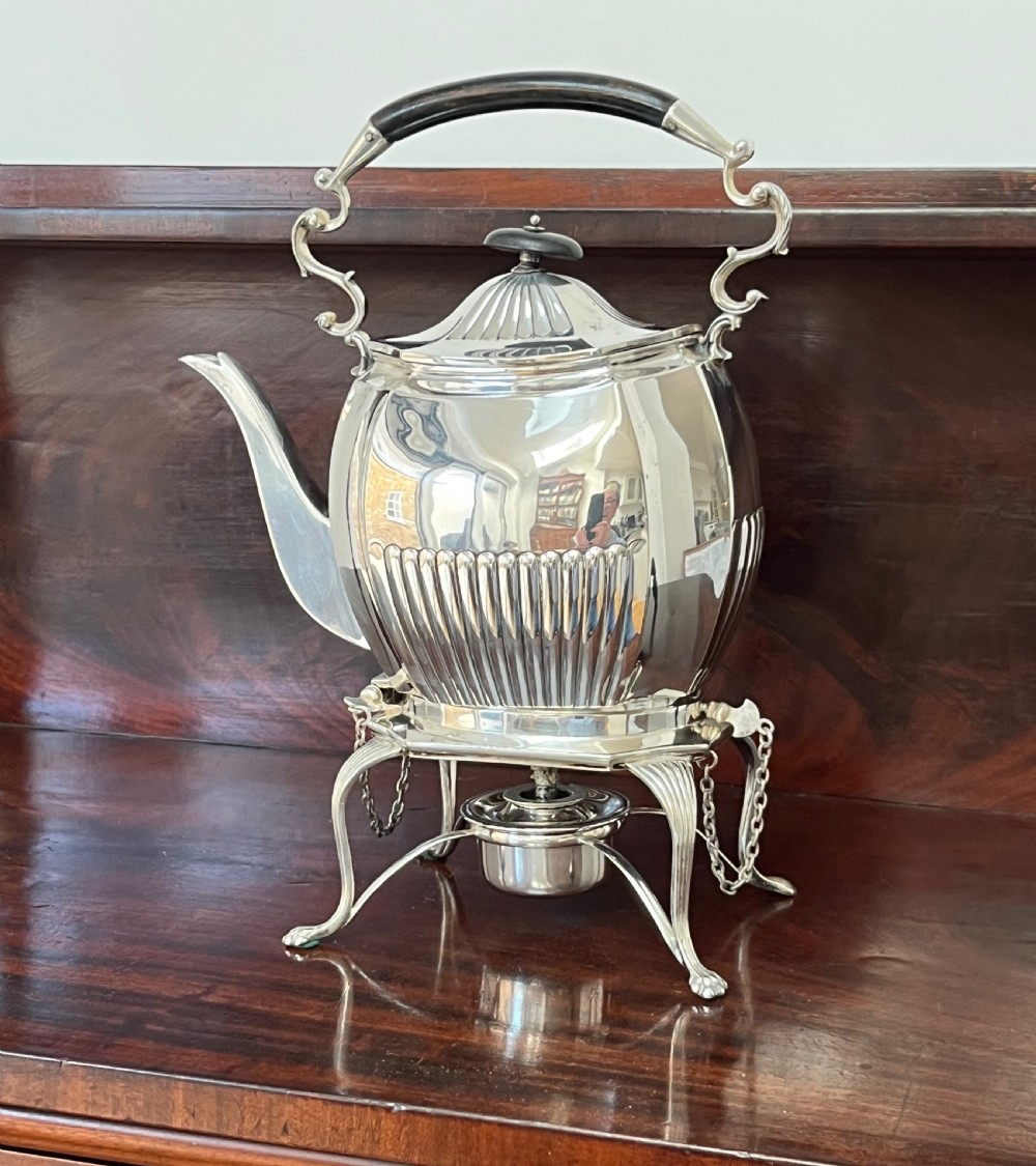 A silver-plated spirit kettle with a fluted lower body, dark wooden handle, gooseneck spout, and matching stand containing an alcohol burner below. View XIV