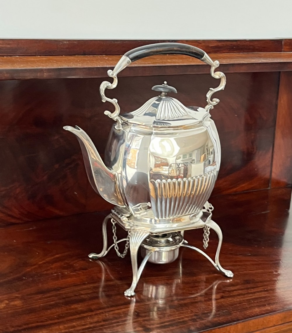 A silver-plated spirit kettle with a fluted lower body, dark wooden handle, gooseneck spout, and matching stand containing an alcohol burner below. View XV