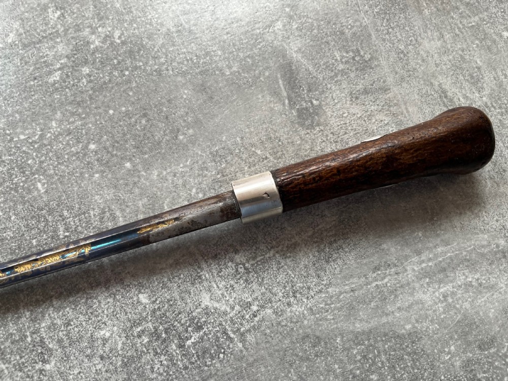 A late 19th-century dark hazel wood walking stick with a curved handle, silver collar, upper eyelet detail, and a metallic ferrule base. View V