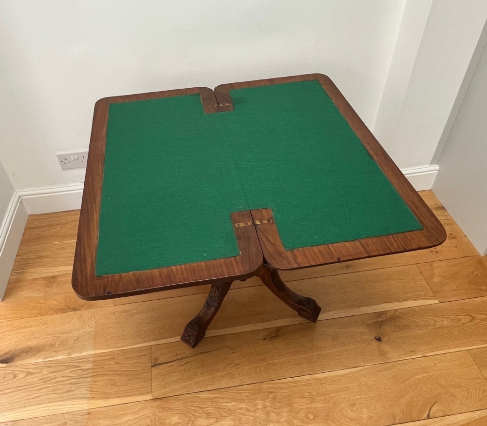 A Victorian burr walnut card table with an unfolded green baize surface resting on a carved pedestal base.