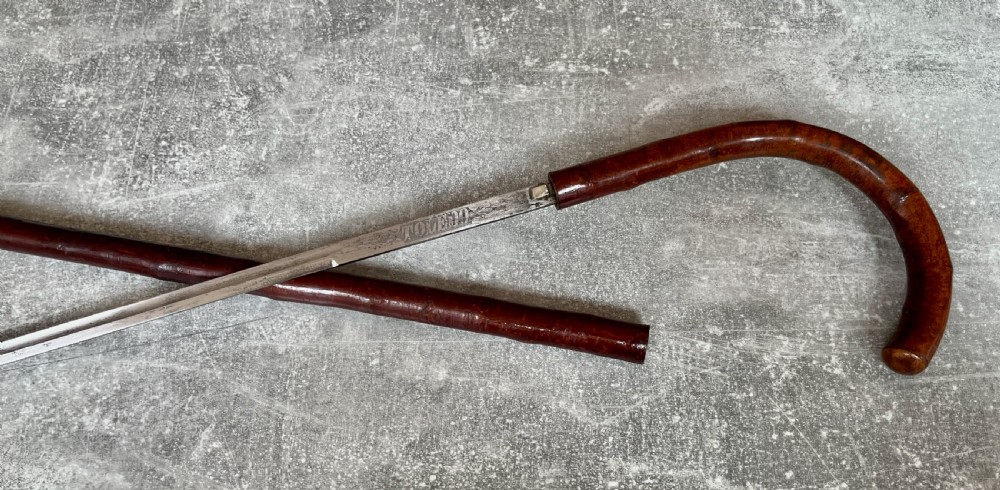 An antique cherrywood sword stick featuring a curved crook handle, a dark polished wood shaft, and a drawn steel blade with etched markings. View VII
