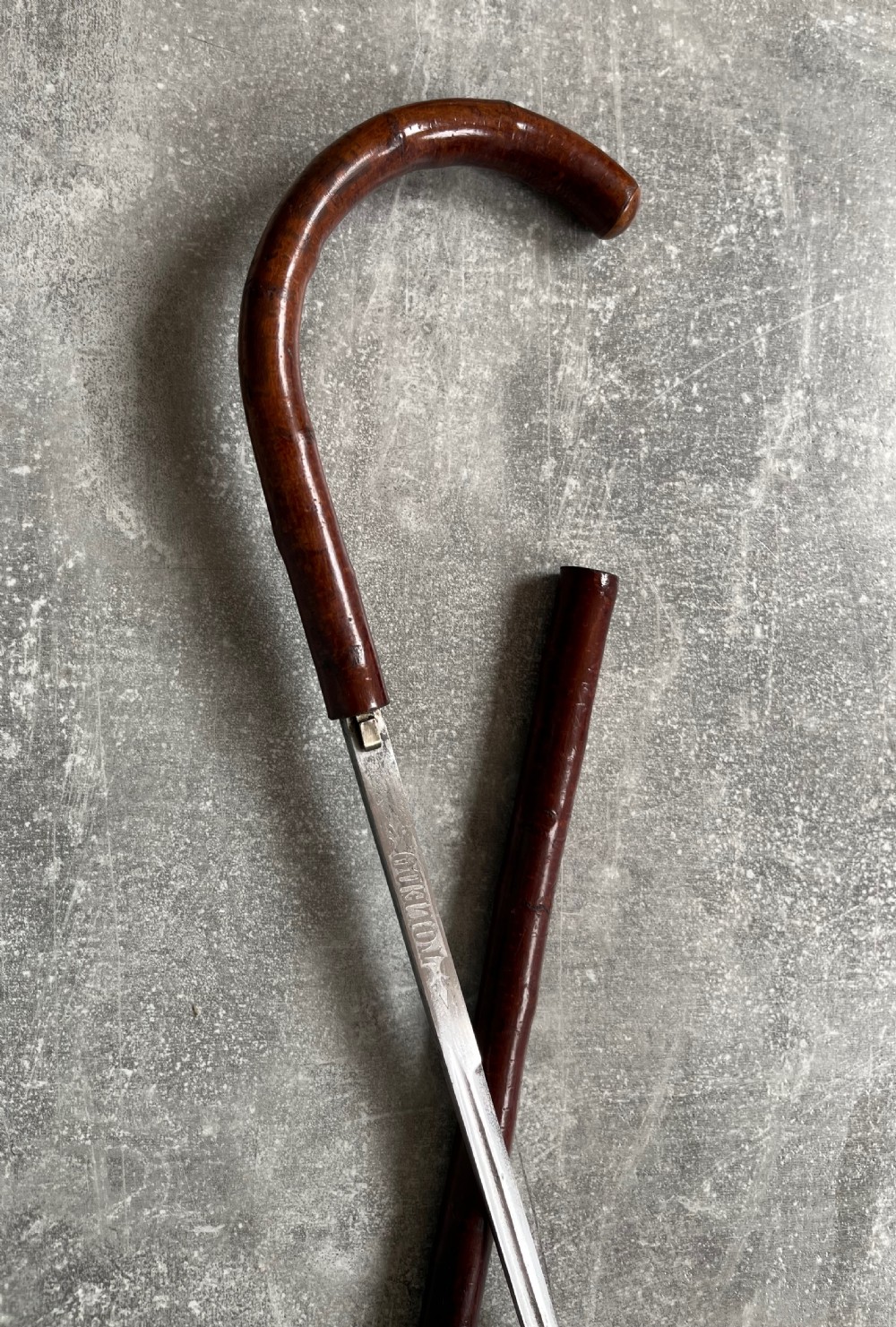 An antique cherrywood sword stick featuring a curved crook handle, a dark polished wood shaft, and a drawn steel blade with etched markings. View IX