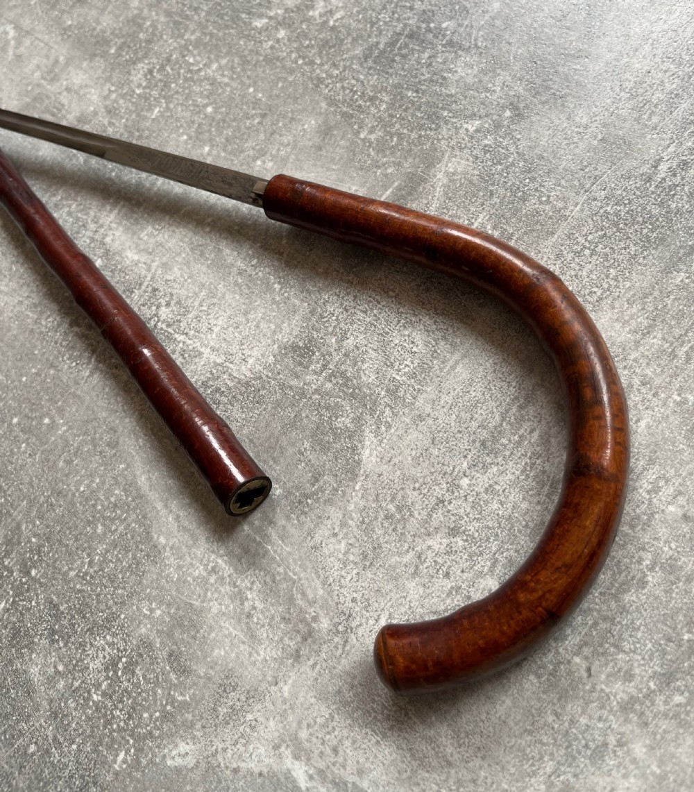 An antique cherrywood sword stick featuring a curved crook handle, a dark polished wood shaft, and a drawn steel blade with etched markings. View XII
