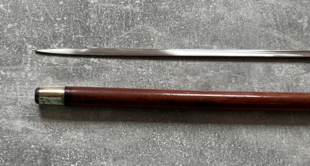 An antique brown Malacca wood walking stick with a curved crook handle, shown unsheathed to reveal an etched steel Toledo blade alongside its wooden sheath. View VI
