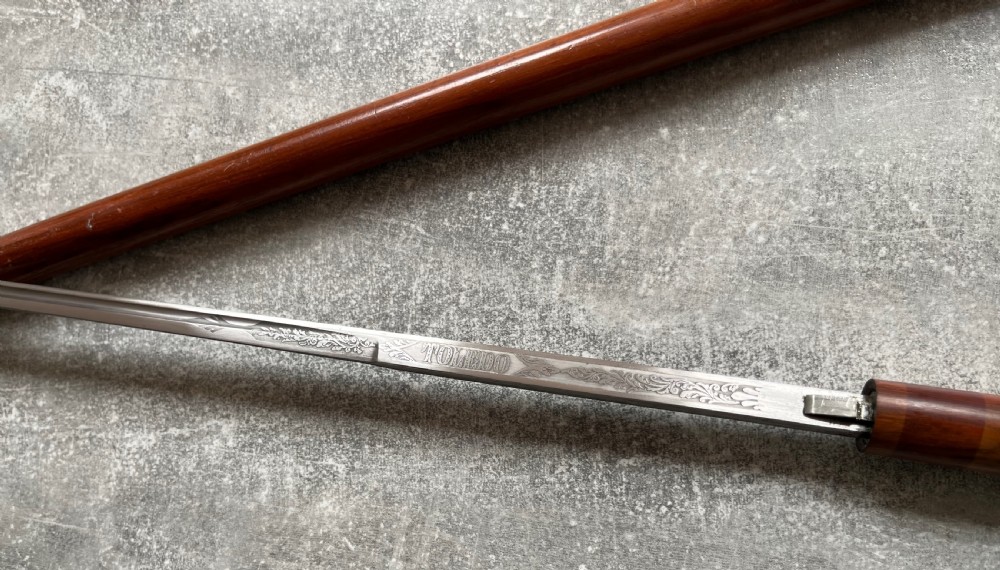 An antique brown Malacca wood walking stick with a curved crook handle, shown unsheathed to reveal an etched steel Toledo blade alongside its wooden sheath. View IX