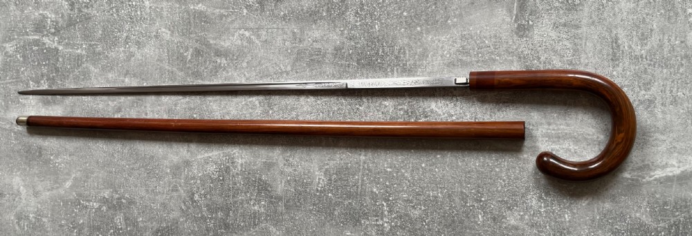 An antique brown Malacca wood walking stick with a curved crook handle, shown unsheathed to reveal an etched steel Toledo blade alongside its wooden sheath. View XIV
