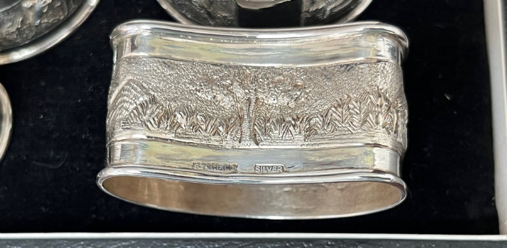 A cased set of six silver napkin rings with embossed relief scenes inside a black silk and velvet box. View II