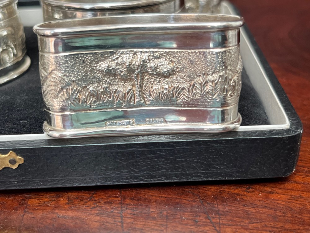 A cased set of six silver napkin rings with embossed relief scenes inside a black silk and velvet box. View V