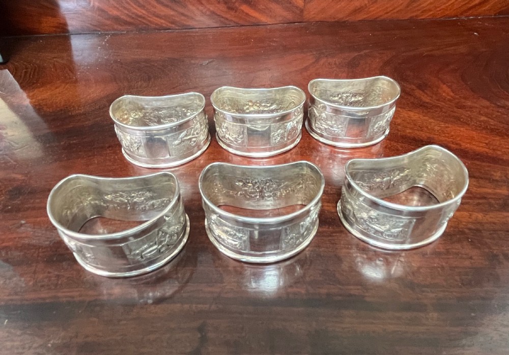 A cased set of six silver napkin rings with embossed relief scenes inside a black silk and velvet box. View VIII