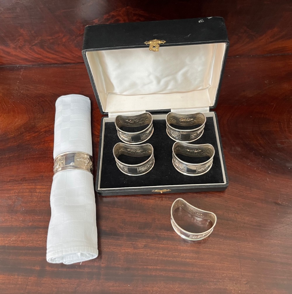 A cased set of six silver napkin rings with embossed relief scenes inside a black silk and velvet box. View IX
