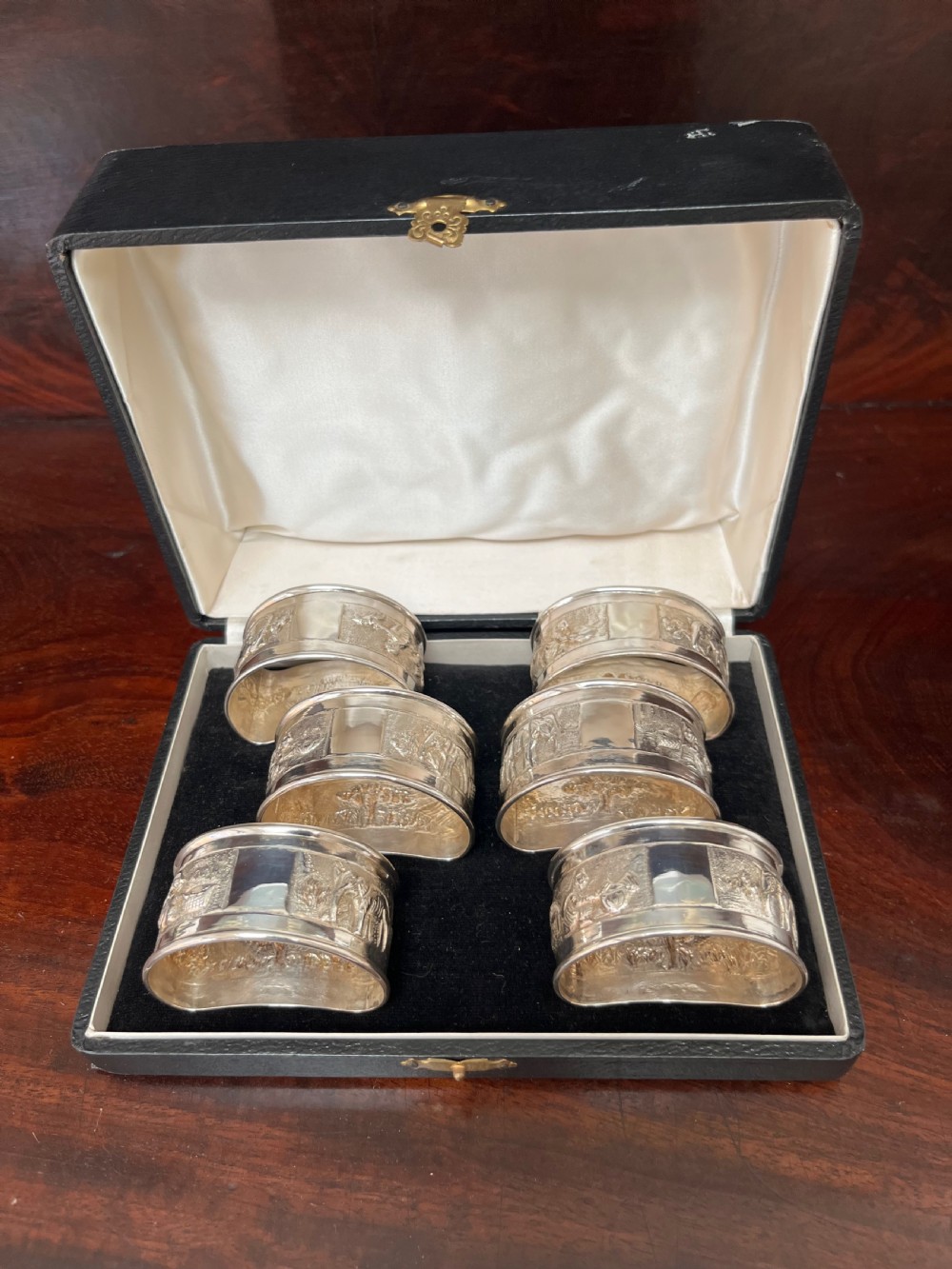 A cased set of six silver napkin rings with embossed relief scenes inside a black silk and velvet box. View XI