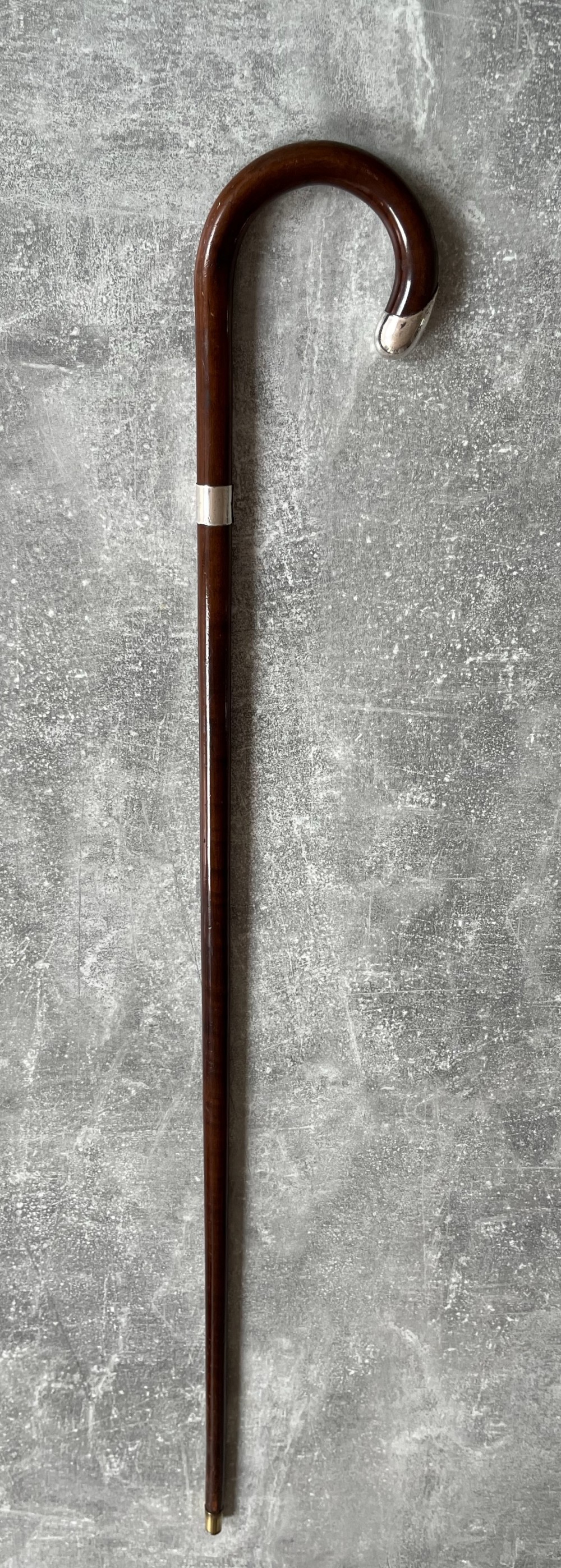 A dark brown polished hardwood walking stick featuring a curved crook handle with silver mounts and a metal ferrule at the tip.