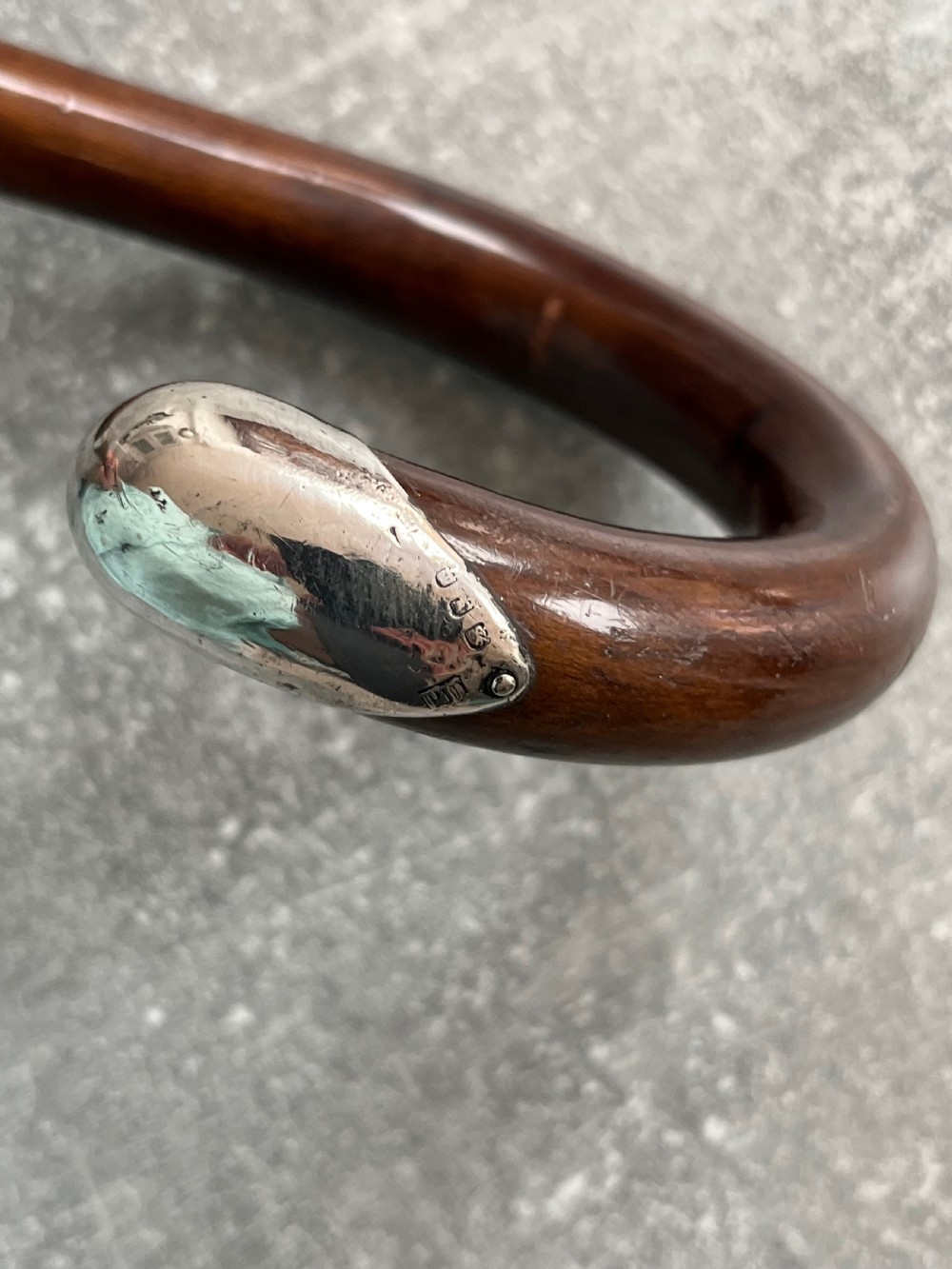 A dark brown polished hardwood walking stick featuring a curved crook handle with silver mounts and a metal ferrule at the tip. View V