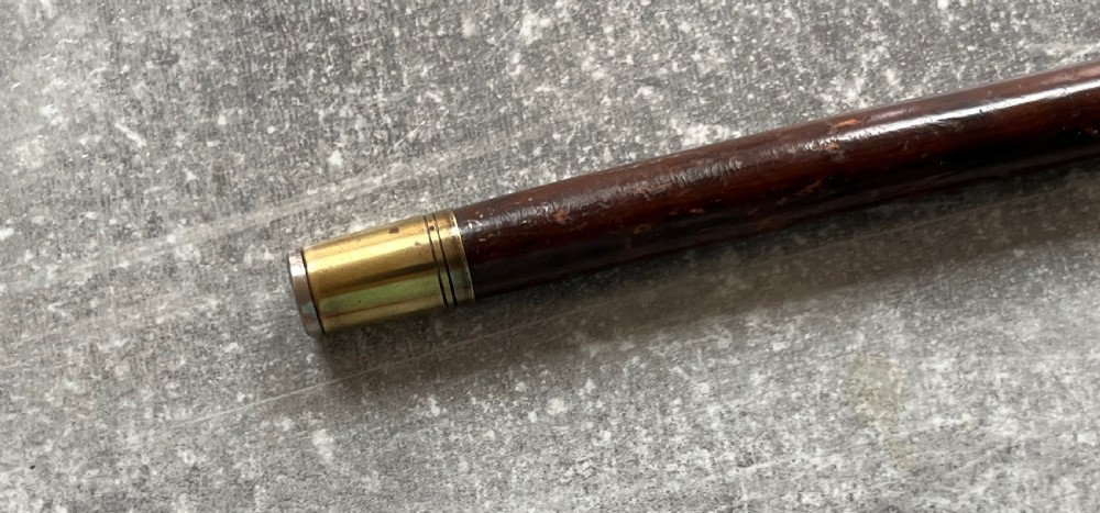 A dark brown polished hardwood walking stick featuring a curved crook handle with silver mounts and a metal ferrule at the tip. View VI