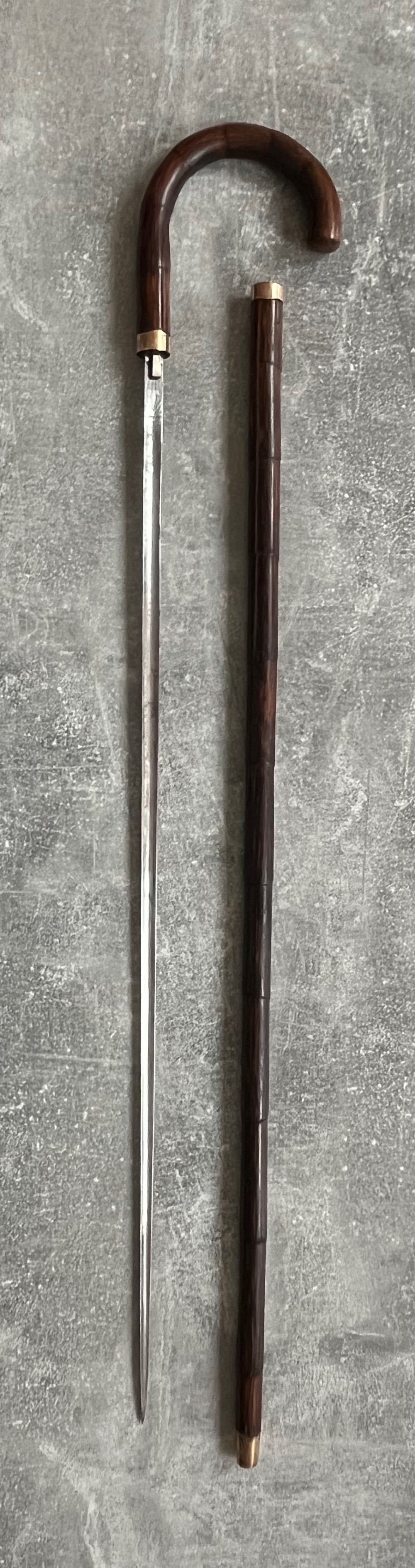A dark wood walking stick featuring a crook handle and faux bamboo carved nodes, unsheathed to reveal a long steel blade alongside its wooden casing.