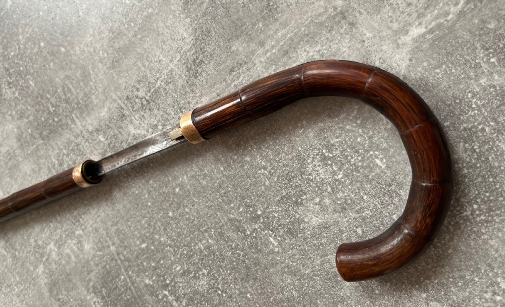 A dark wood walking stick featuring a crook handle and faux bamboo carved nodes, unsheathed to reveal a long steel blade alongside its wooden casing. View III
