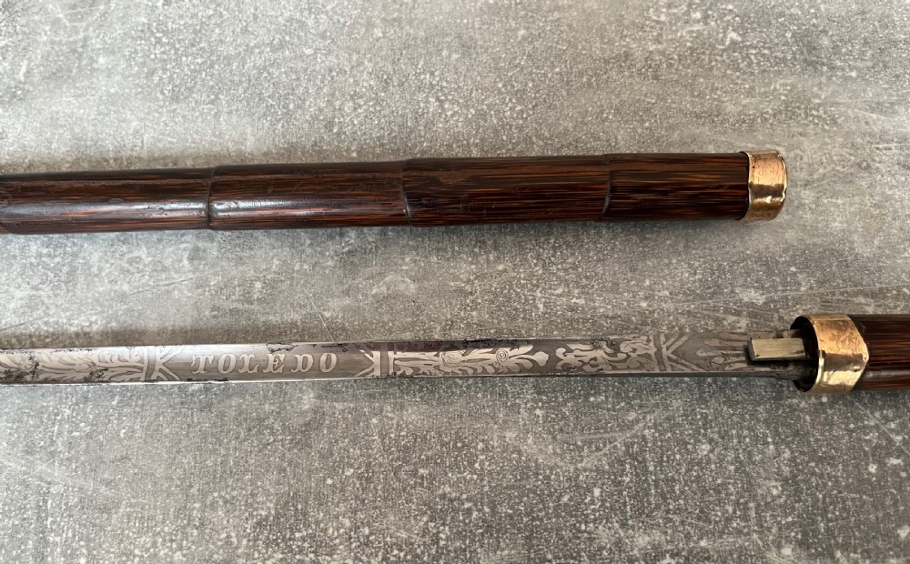 A dark wood walking stick featuring a crook handle and faux bamboo carved nodes, unsheathed to reveal a long steel blade alongside its wooden casing. View V