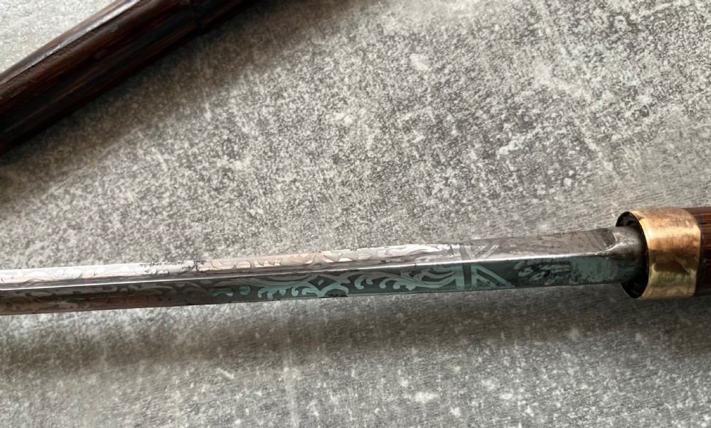 A dark wood walking stick featuring a crook handle and faux bamboo carved nodes, unsheathed to reveal a long steel blade alongside its wooden casing. View VII