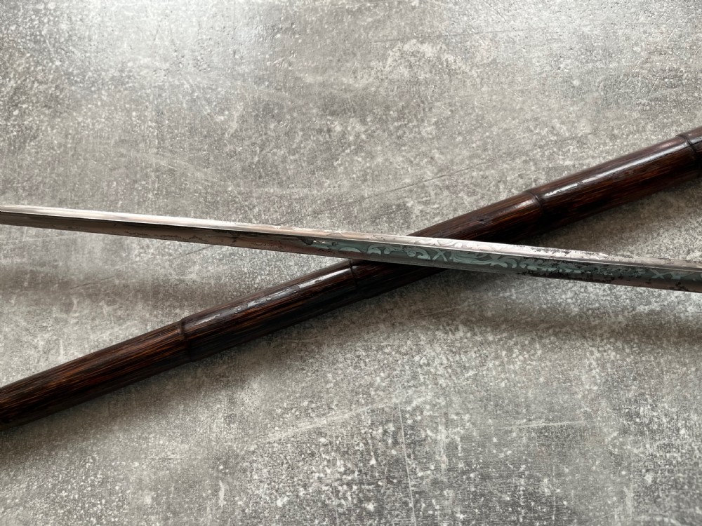 A dark wood walking stick featuring a crook handle and faux bamboo carved nodes, unsheathed to reveal a long steel blade alongside its wooden casing. View VIII