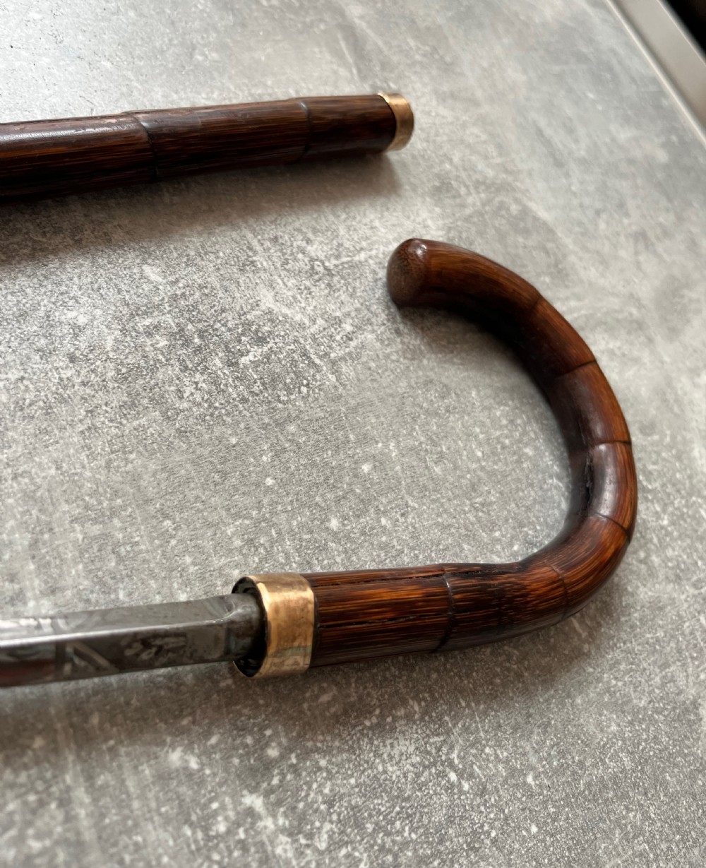 A dark wood walking stick featuring a crook handle and faux bamboo carved nodes, unsheathed to reveal a long steel blade alongside its wooden casing. View XII
