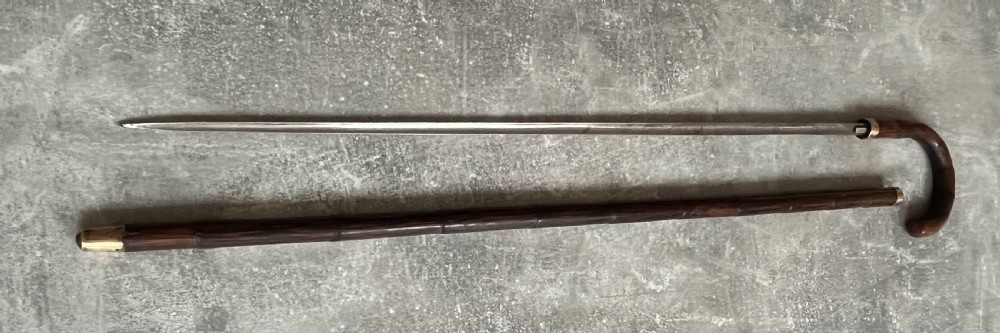 A dark wood walking stick featuring a crook handle and faux bamboo carved nodes, unsheathed to reveal a long steel blade alongside its wooden casing. View XIV