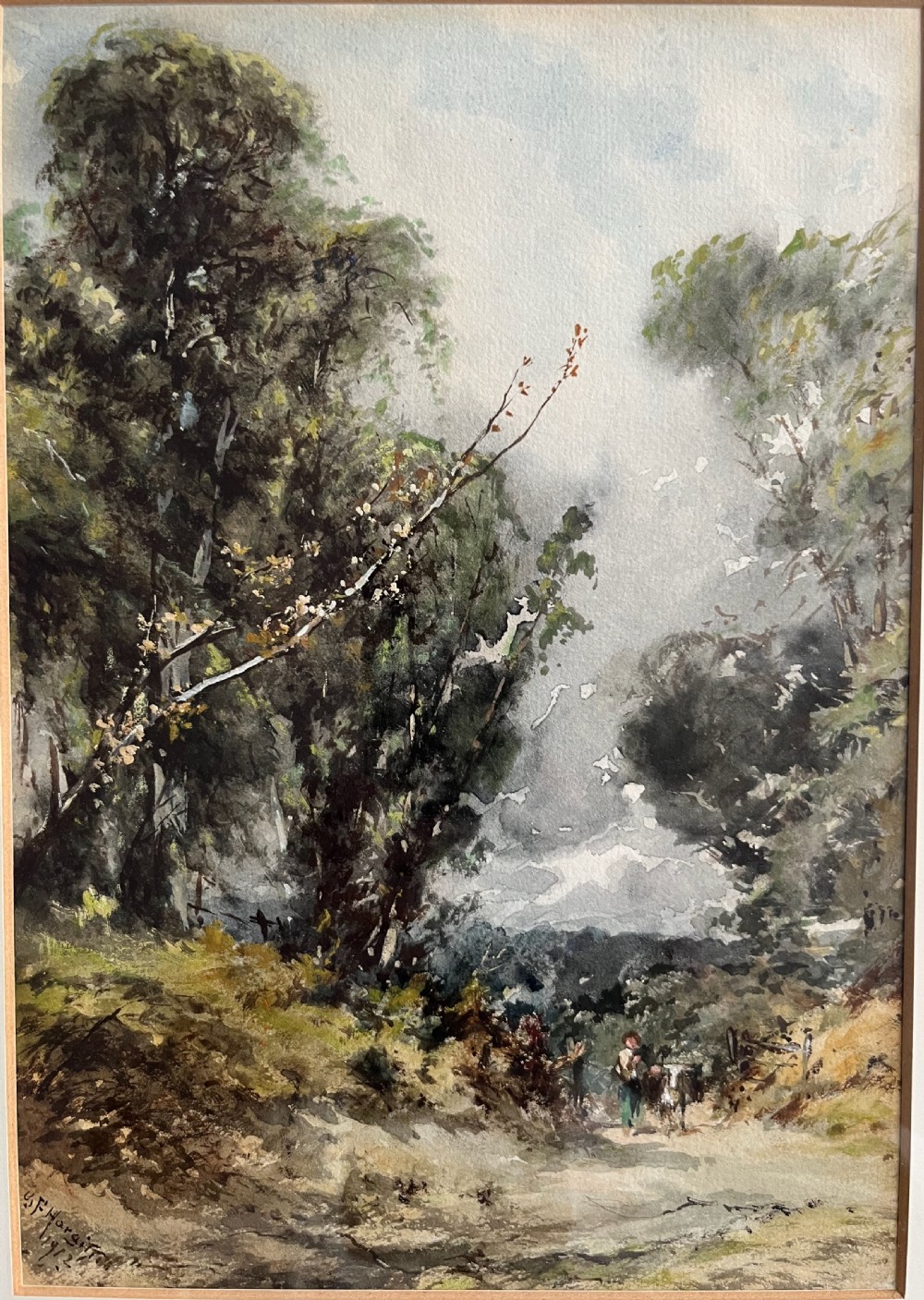A framed 19th-century watercolour painting depicting a wooded countryside path under a clouded sky, mounted in a lined cream mat and narrow gilt-trimmed wooden frame. View II