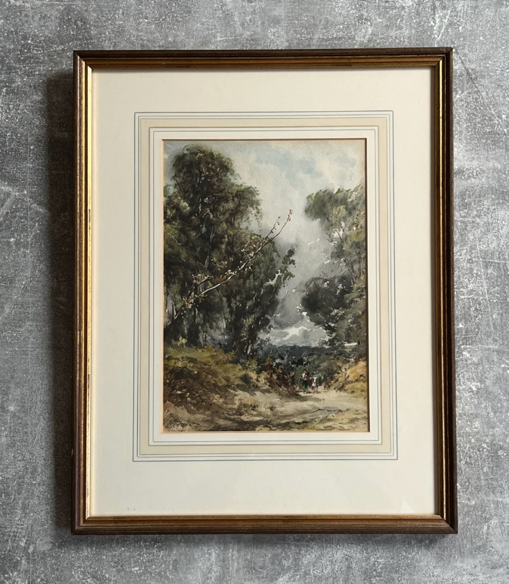 A framed 19th-century watercolour painting depicting a wooded countryside path under a clouded sky, mounted in a lined cream mat and narrow gilt-trimmed wooden frame. View VII