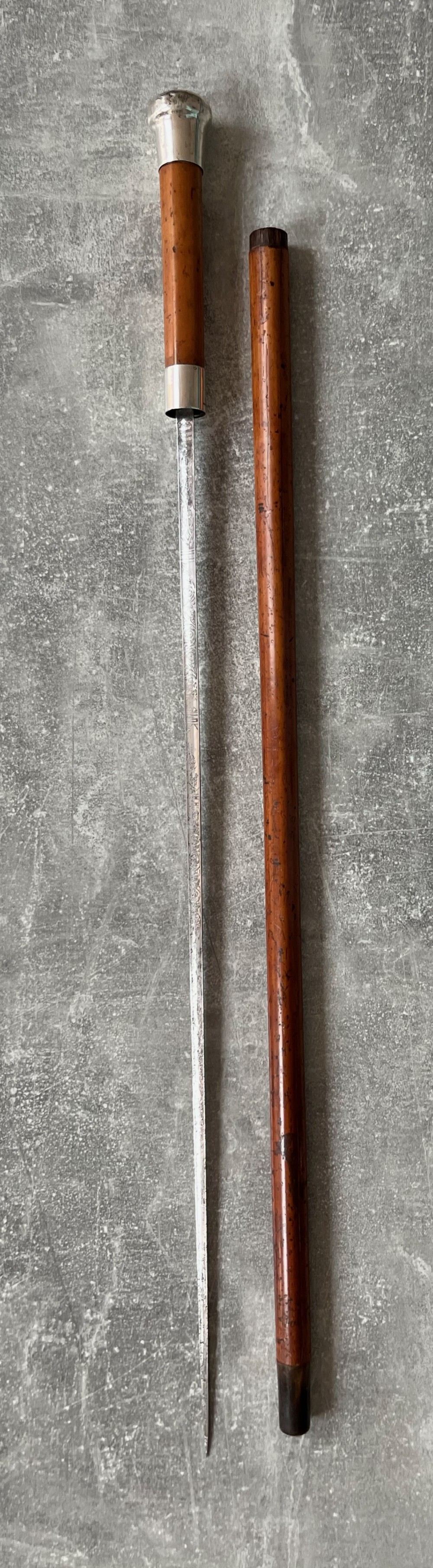 An antique malacca cane sword stick featuring a hallmarked silver pommel collar and an etched steel blade alongside its wooden sheath.