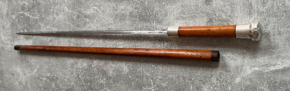 An antique malacca cane sword stick featuring a hallmarked silver pommel collar and an etched steel blade alongside its wooden sheath. View III