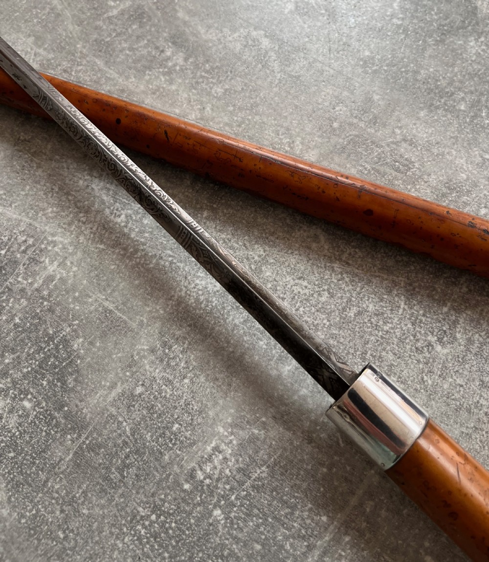 An antique malacca cane sword stick featuring a hallmarked silver pommel collar and an etched steel blade alongside its wooden sheath. View VIII