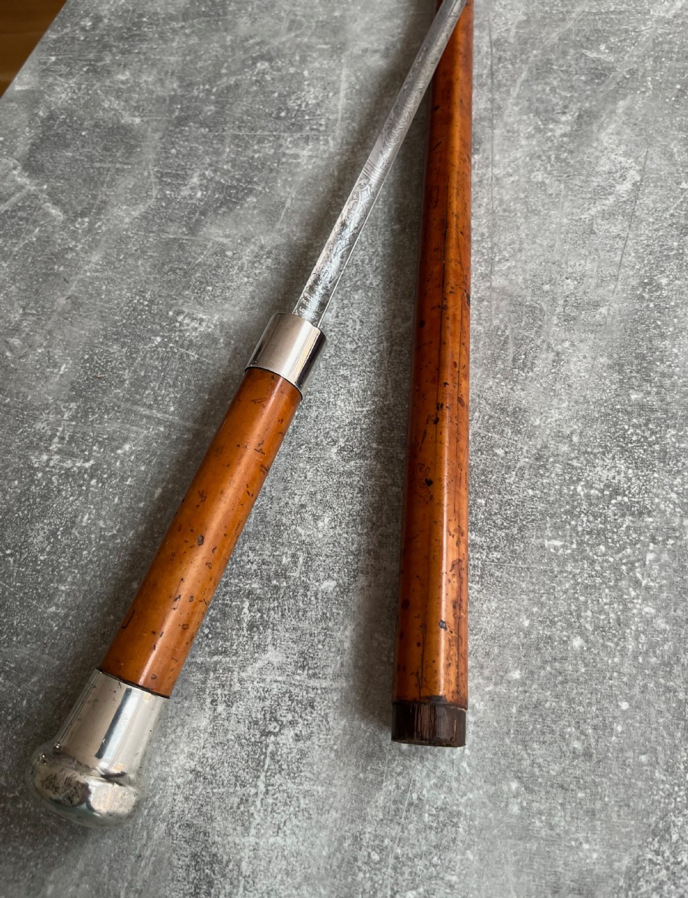 An antique malacca cane sword stick featuring a hallmarked silver pommel collar and an etched steel blade alongside its wooden sheath. View IX