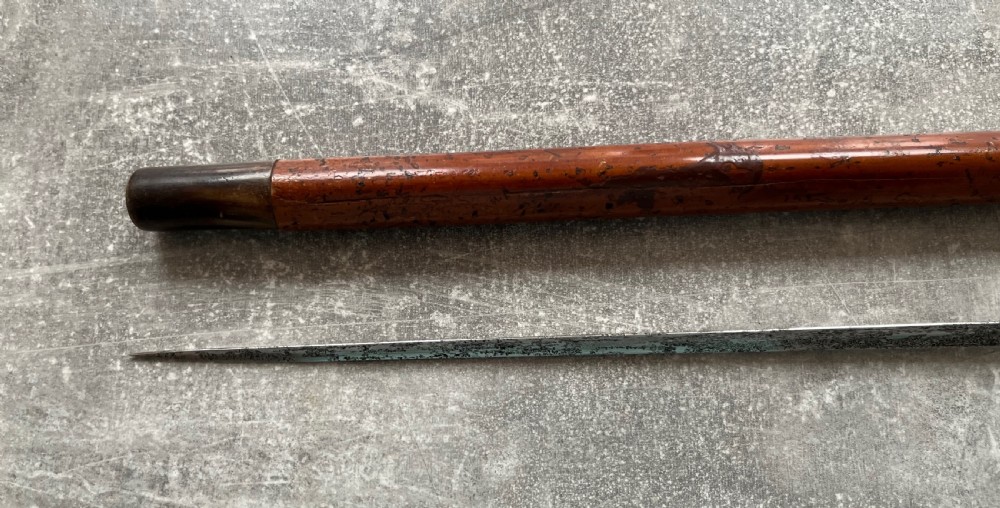 An antique malacca cane sword stick featuring a hallmarked silver pommel collar and an etched steel blade alongside its wooden sheath. View X