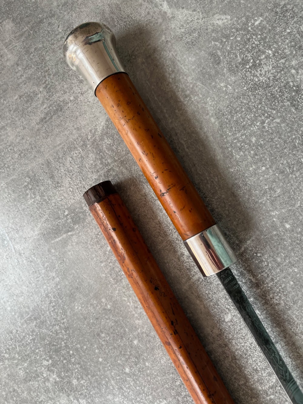 An antique malacca cane sword stick featuring a hallmarked silver pommel collar and an etched steel blade alongside its wooden sheath. View XI