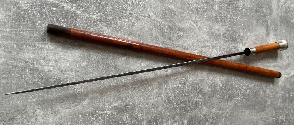 An antique malacca cane sword stick featuring a hallmarked silver pommel collar and an etched steel blade alongside its wooden sheath. View XIII