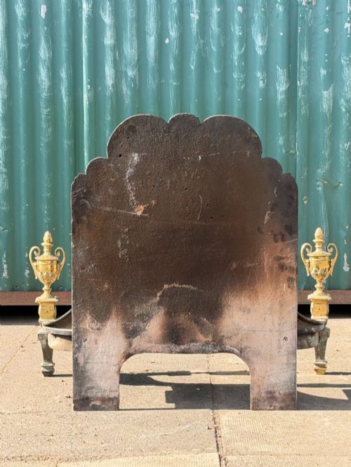 fig 1. A late nineteenth-century George III style fire grate featuring an ornate cast iron fireback with scrollwork and decorative brass urn finials set on tapered brass legs.