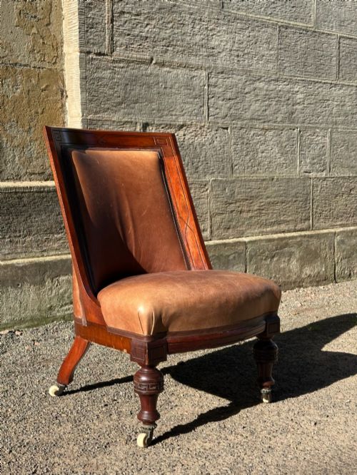 fig 1. A pair of nineteenth-century Greek Revival mahogany armchairs upholstered in warm brown leather with turned front legs on castors and incised geometric detailing.