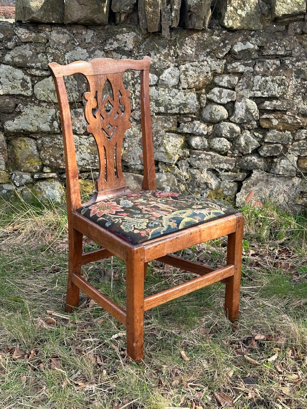 A George III walnut side chair featuring a carved pierced splat back and a floral needlepoint upholstered drop-in seat.