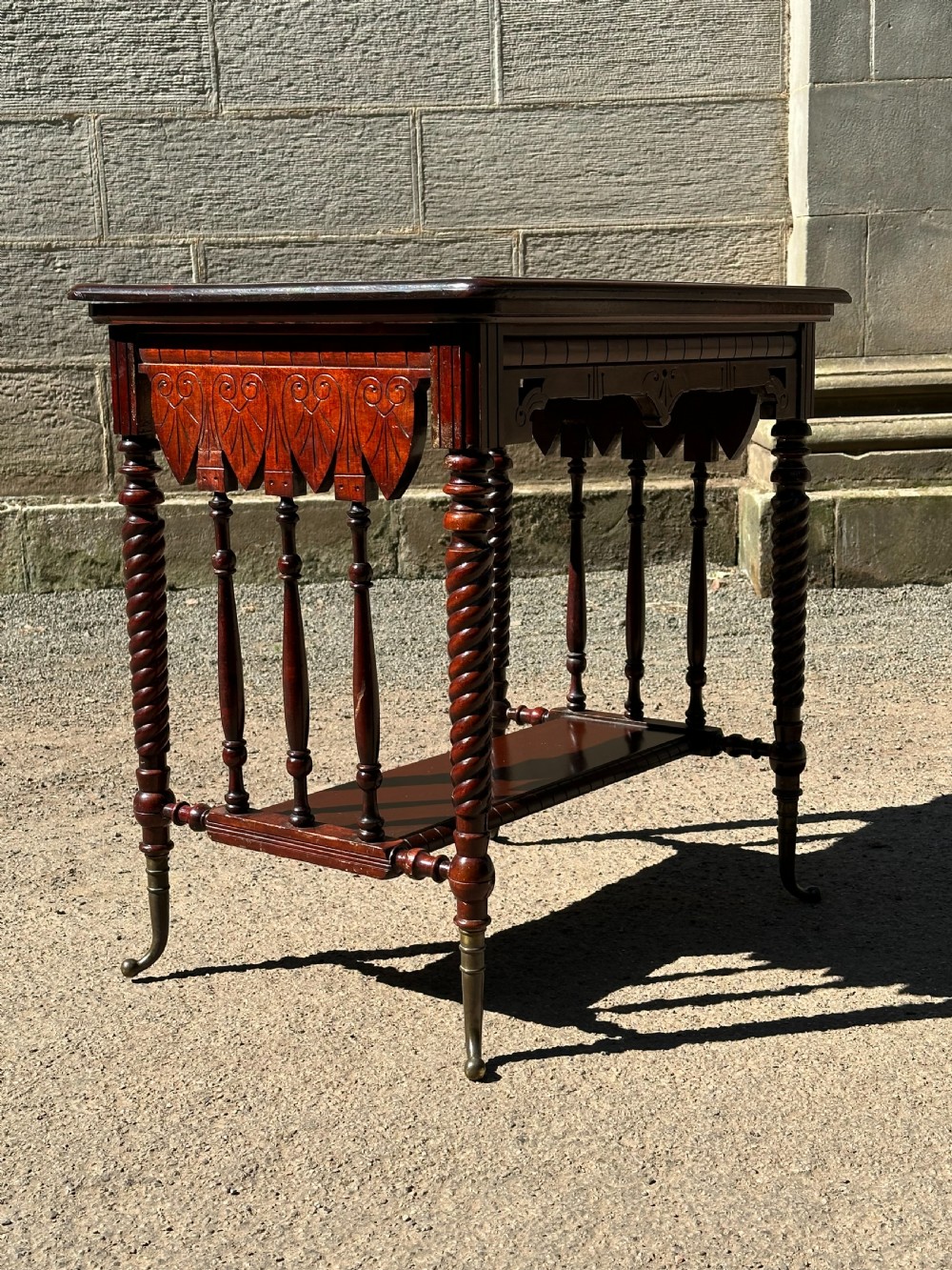 An Aesthetic Movement stained birch centre table featuring barley twist legs, carved foliage aprons, a lower tier with slender spindles, and brass sabots. View II