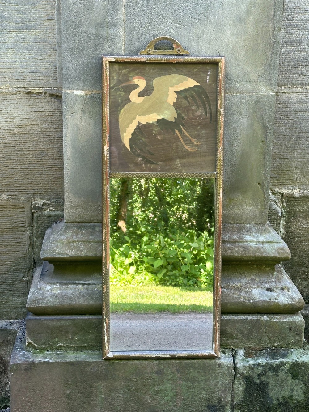 A tall rectangular Art Deco wall mirror featuring an upper wood marquetry panel depicting a crane in flight above a mirror glass section, encased in a silver-gilt frame.