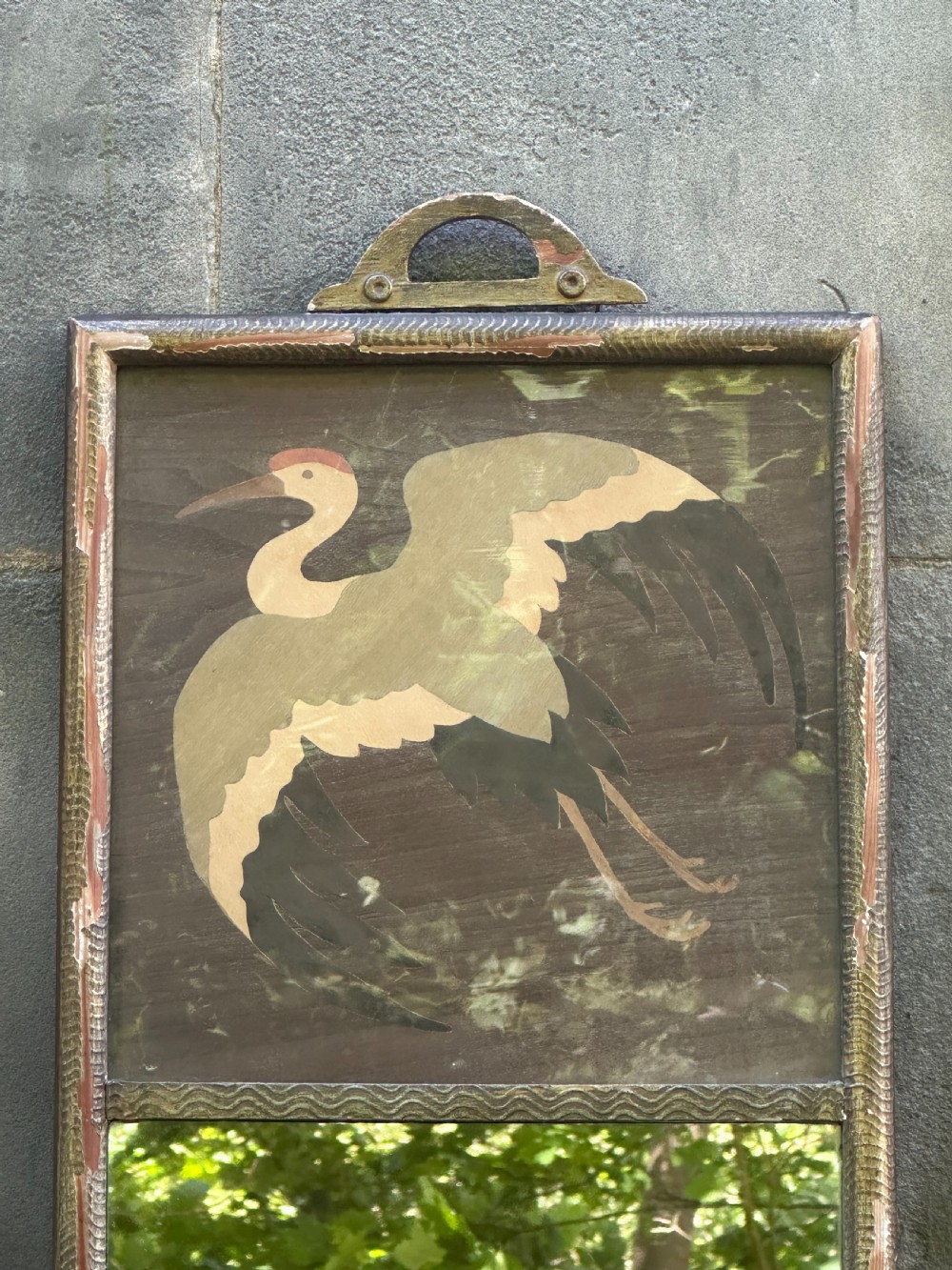 A tall rectangular Art Deco wall mirror featuring an upper wood marquetry panel depicting a crane in flight above a mirror glass section, encased in a silver-gilt frame. View V