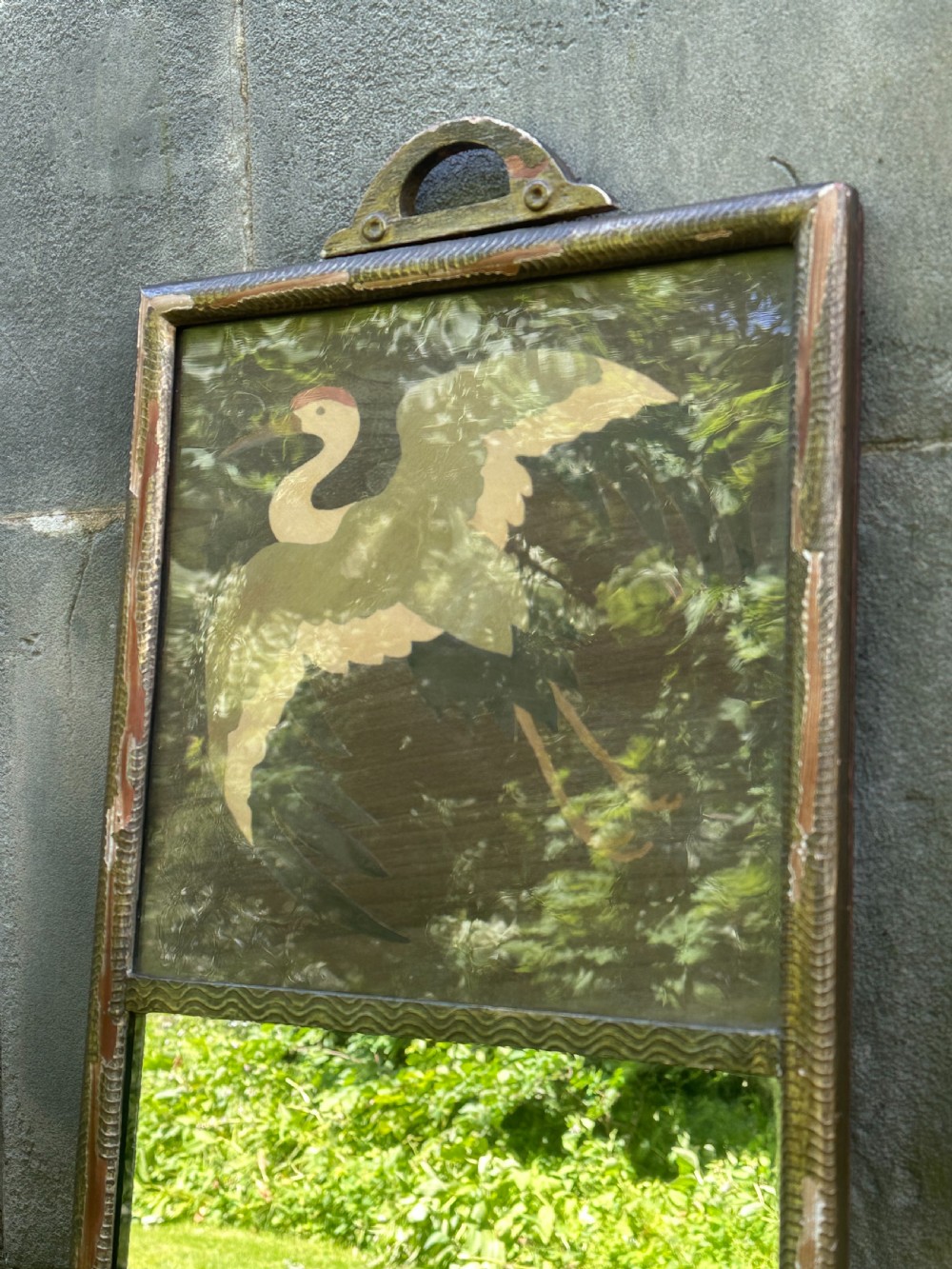A tall rectangular Art Deco wall mirror featuring an upper wood marquetry panel depicting a crane in flight above a mirror glass section, encased in a silver-gilt frame. View VII