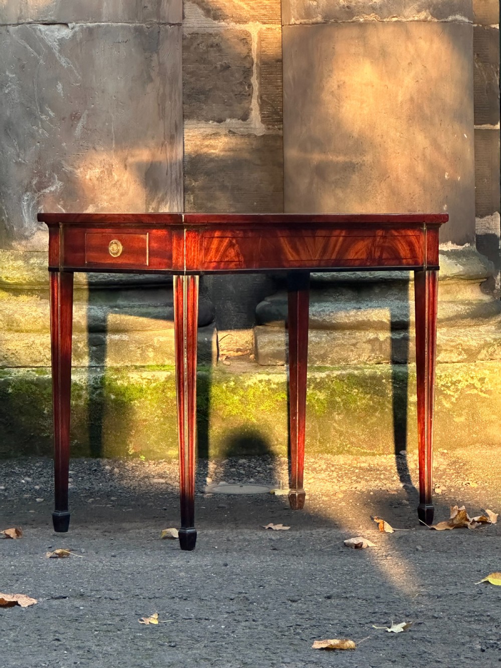 A George III mahogany side table with tapered legs, a flame mahogany veneered frieze, and a brass drawer pull. View II