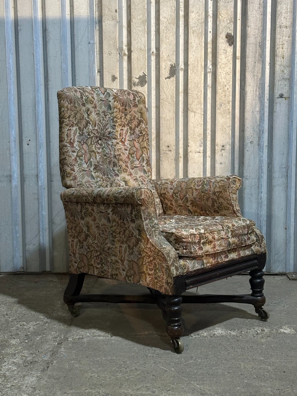 A mid-19th-century English ebonised reclining library armchair with patterned fabric upholstery and turned front legs on brass castors.