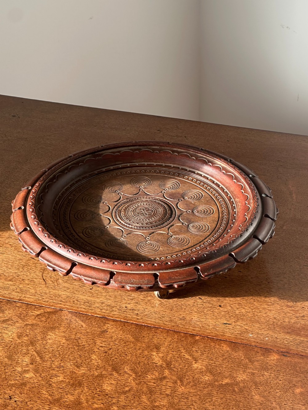 A circular carved mahogany decanter coaster featuring intricate central geometric patterns, a gadrooned rim, and small castors mounted underneath.
