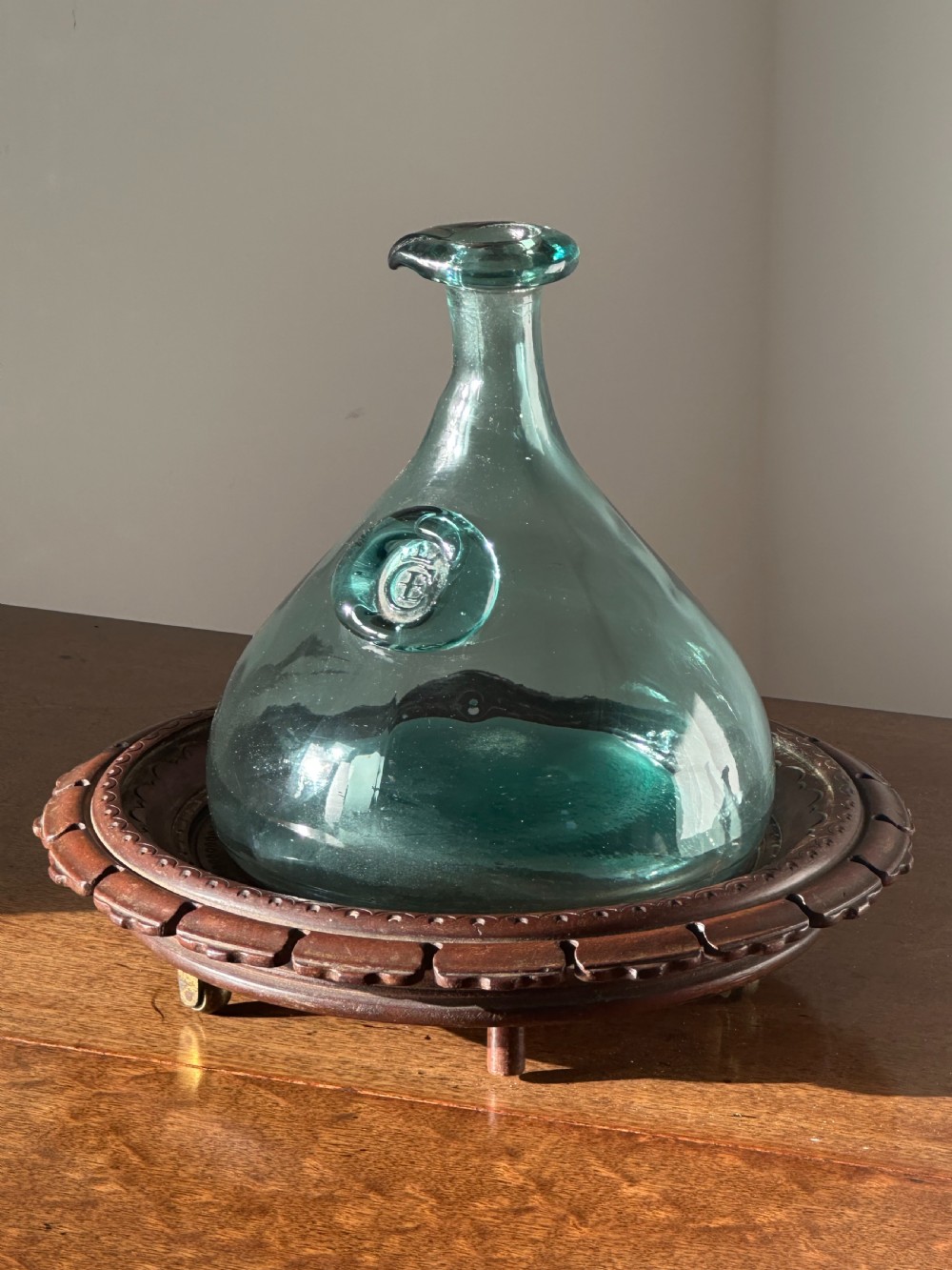 A circular carved mahogany decanter coaster featuring intricate central geometric patterns, a gadrooned rim, and small castors mounted underneath. View III