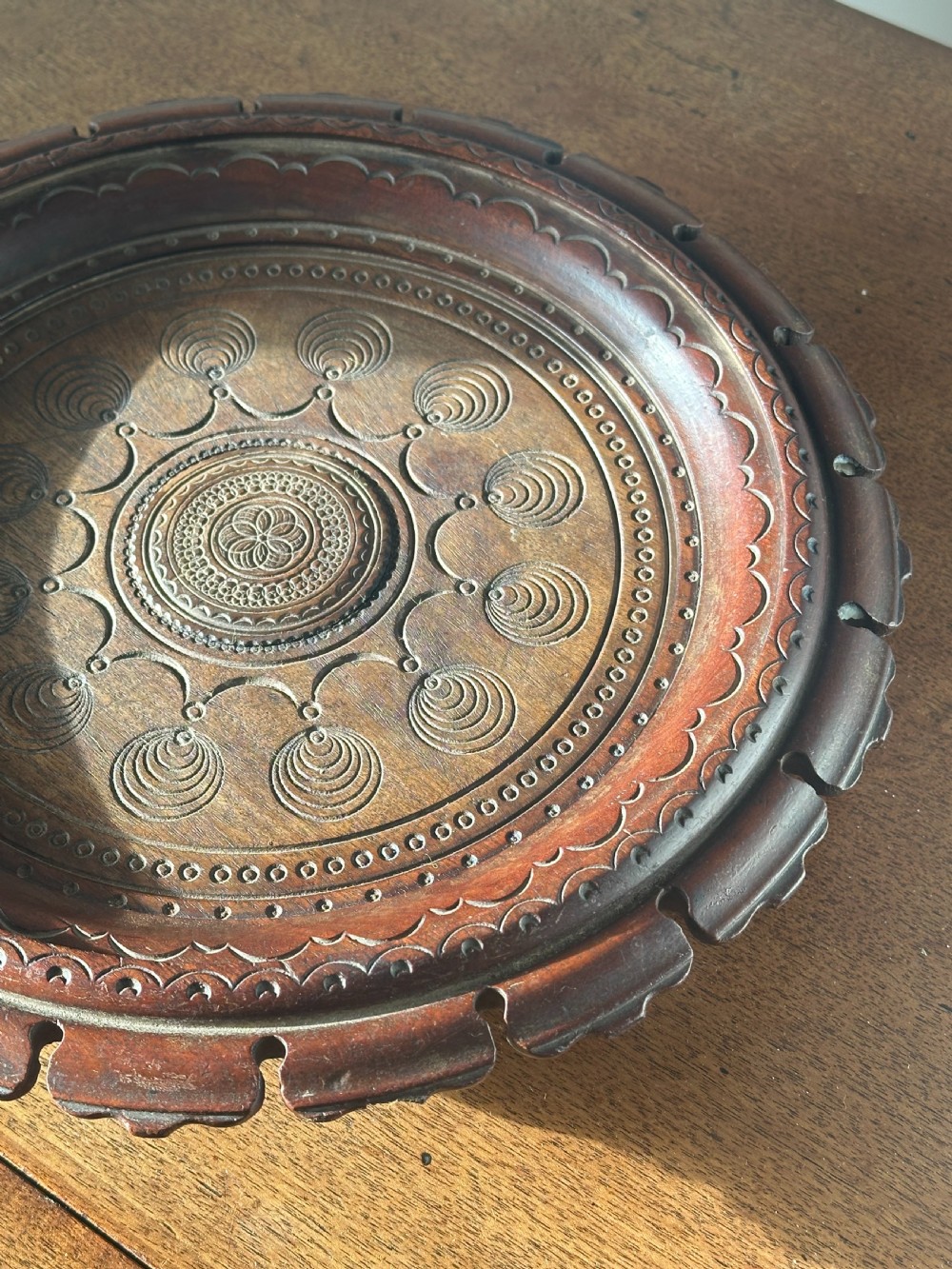 A circular carved mahogany decanter coaster featuring intricate central geometric patterns, a gadrooned rim, and small castors mounted underneath. View V