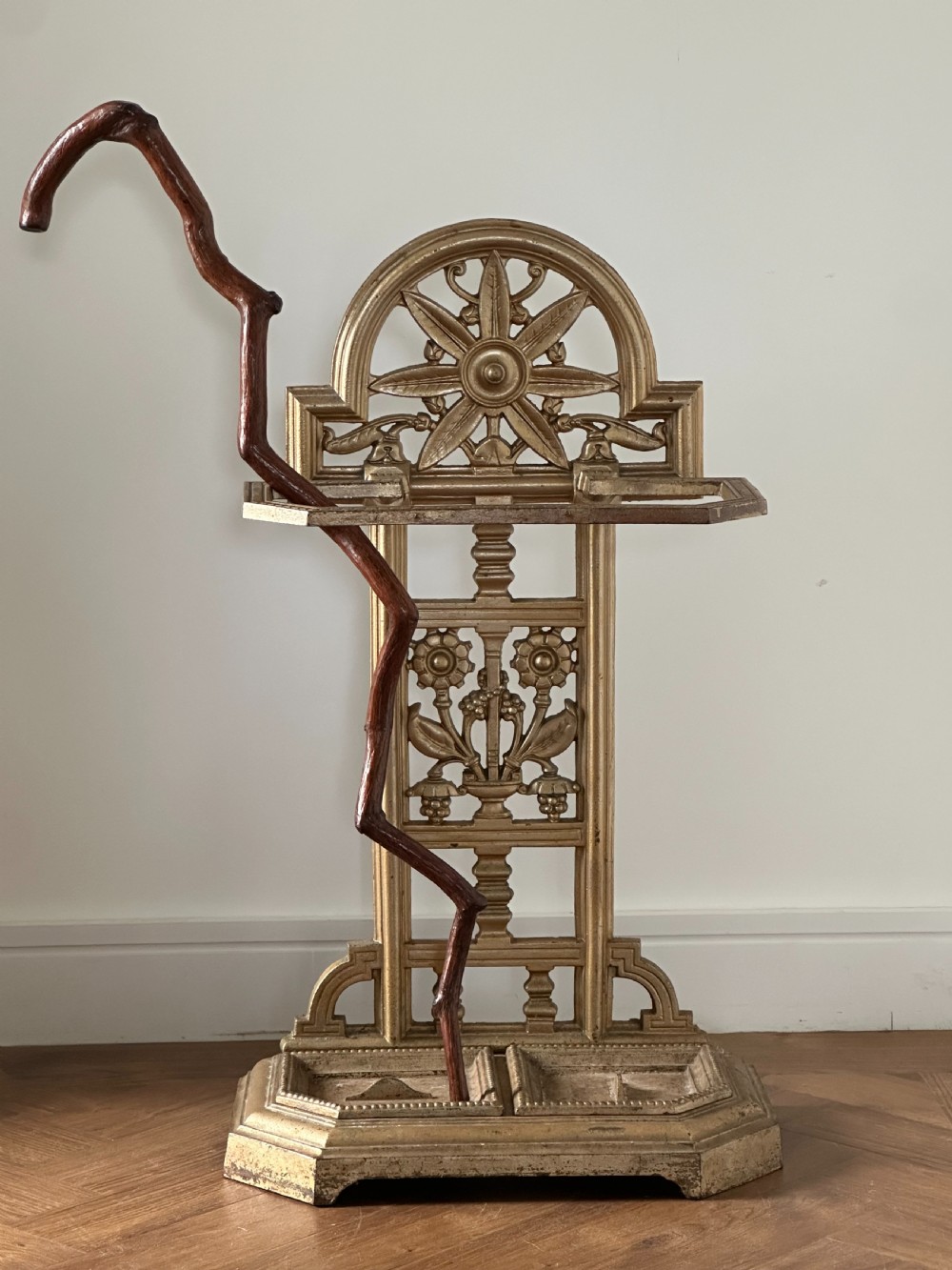 A gold-painted cast iron stick stand featuring a starburst arched cresting, stylised floral central panel, rectangular top ring, and a heavy drip tray base. View X